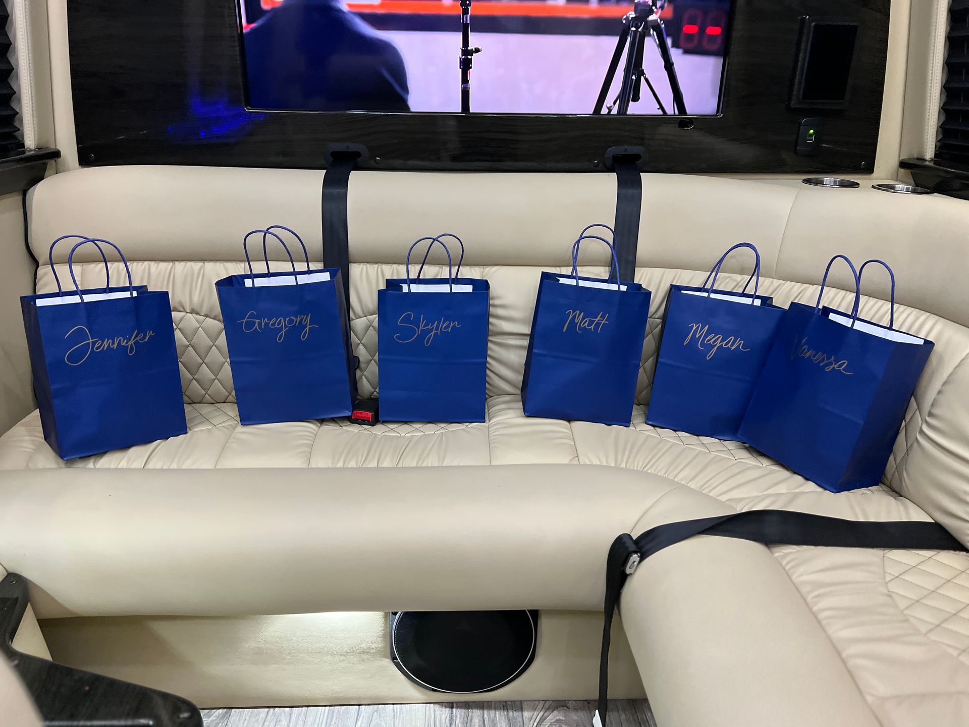 Six blue gift bags with gold lettering on a cream-colored limousine seat.