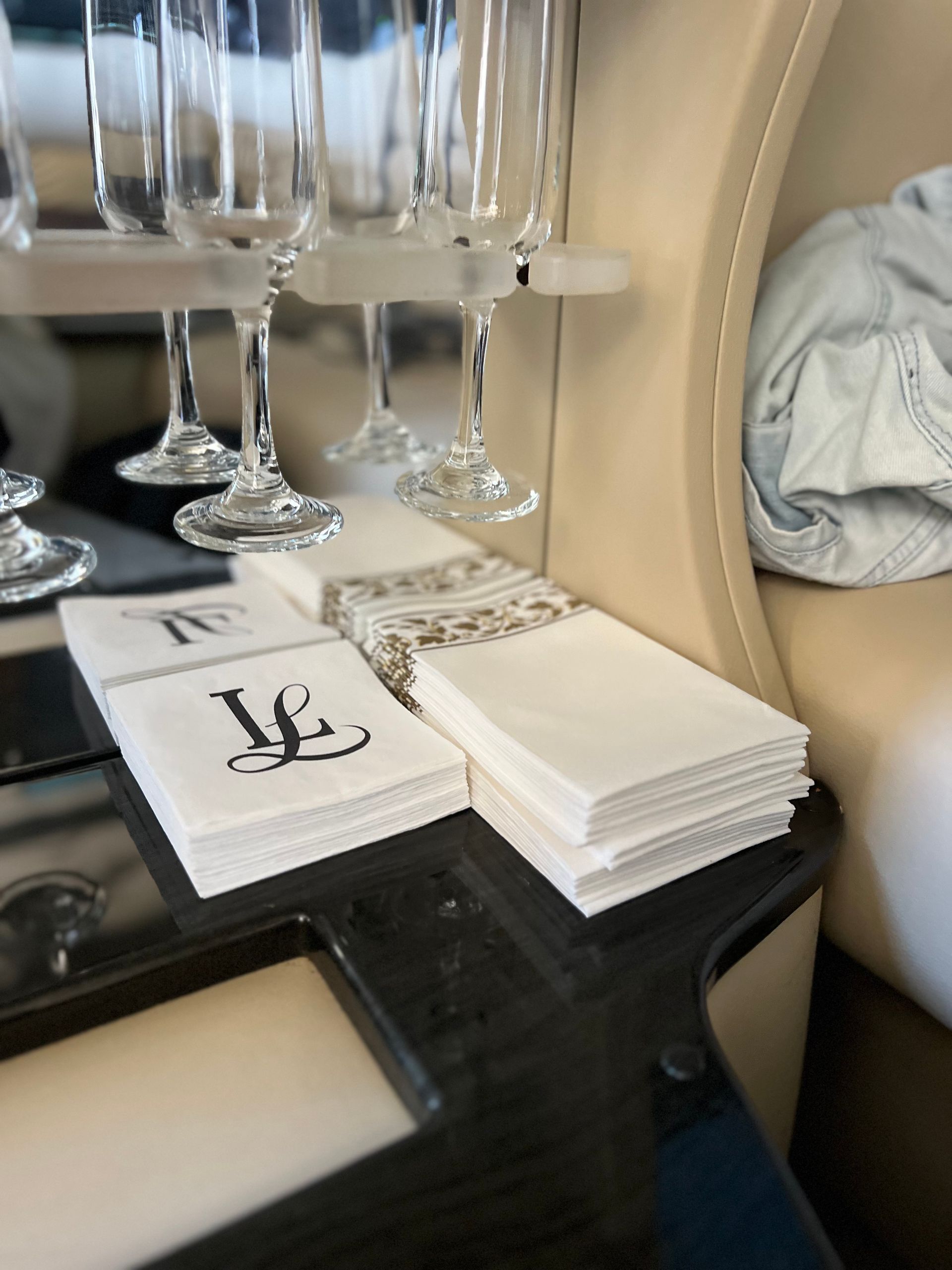 Champagne glasses above a stack of white napkins with decorative borders and initial