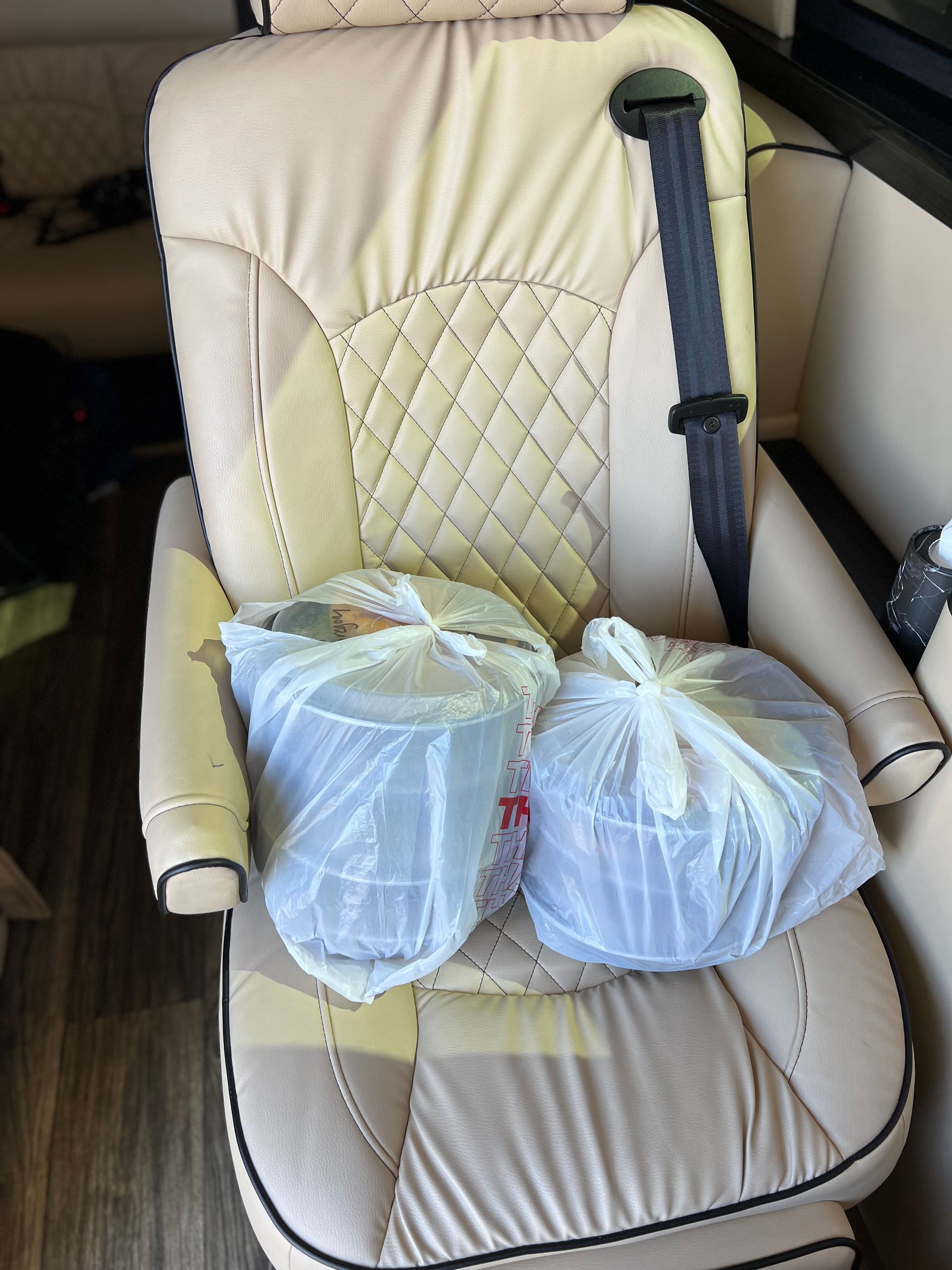 Tan upholstered seat with two wrapped takeout containers. Seatbelt is fastened.