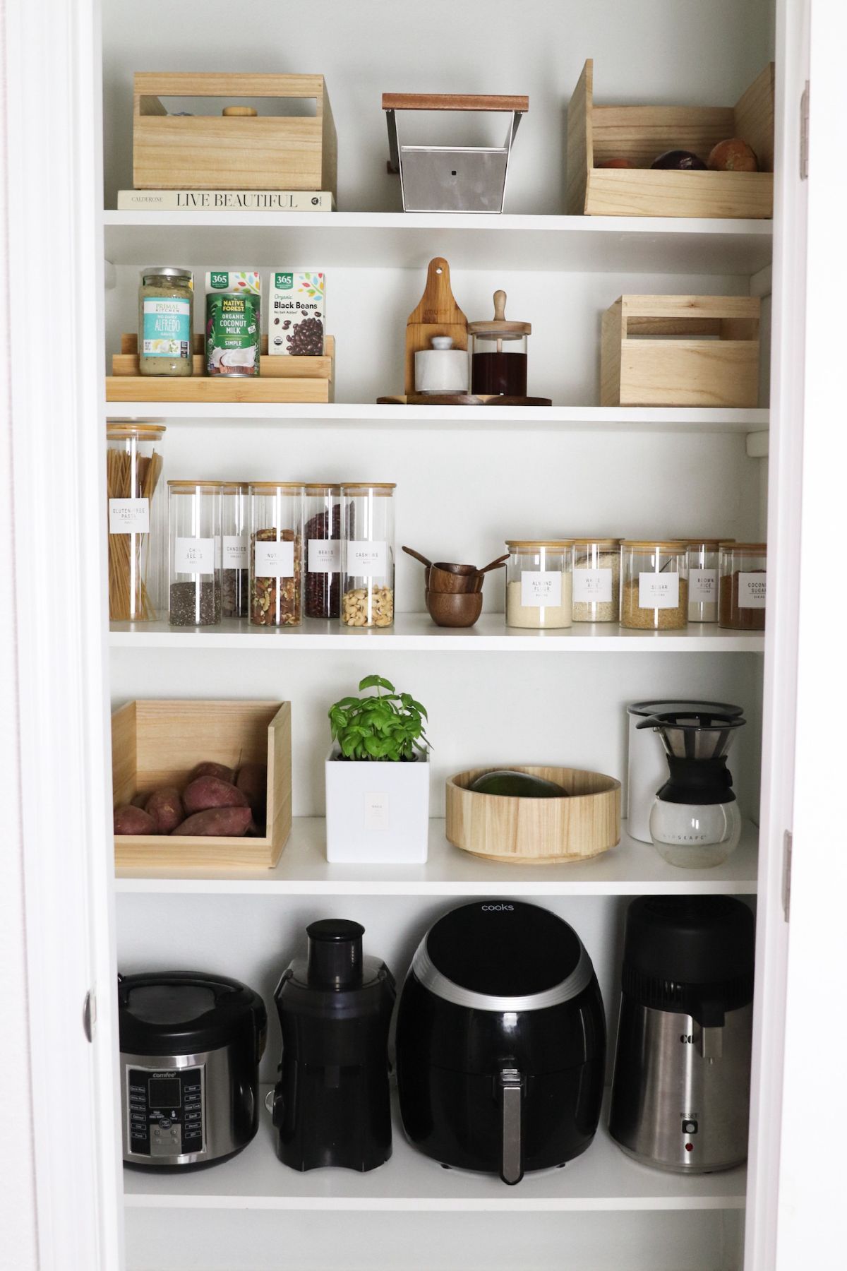 Organized pantry with white shelves and wooden containers holding food items and appliances.