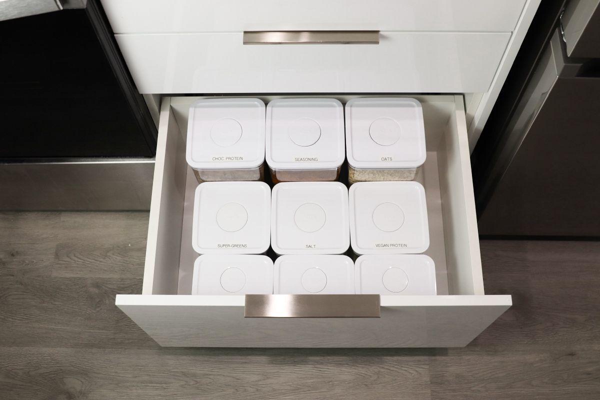White kitchen drawer with six white square containers neatly arranged inside.