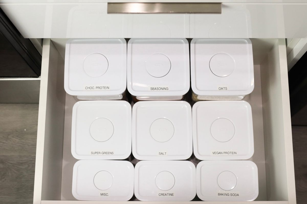 Nine white square containers in a drawer, each labeled with text, organized neatly.