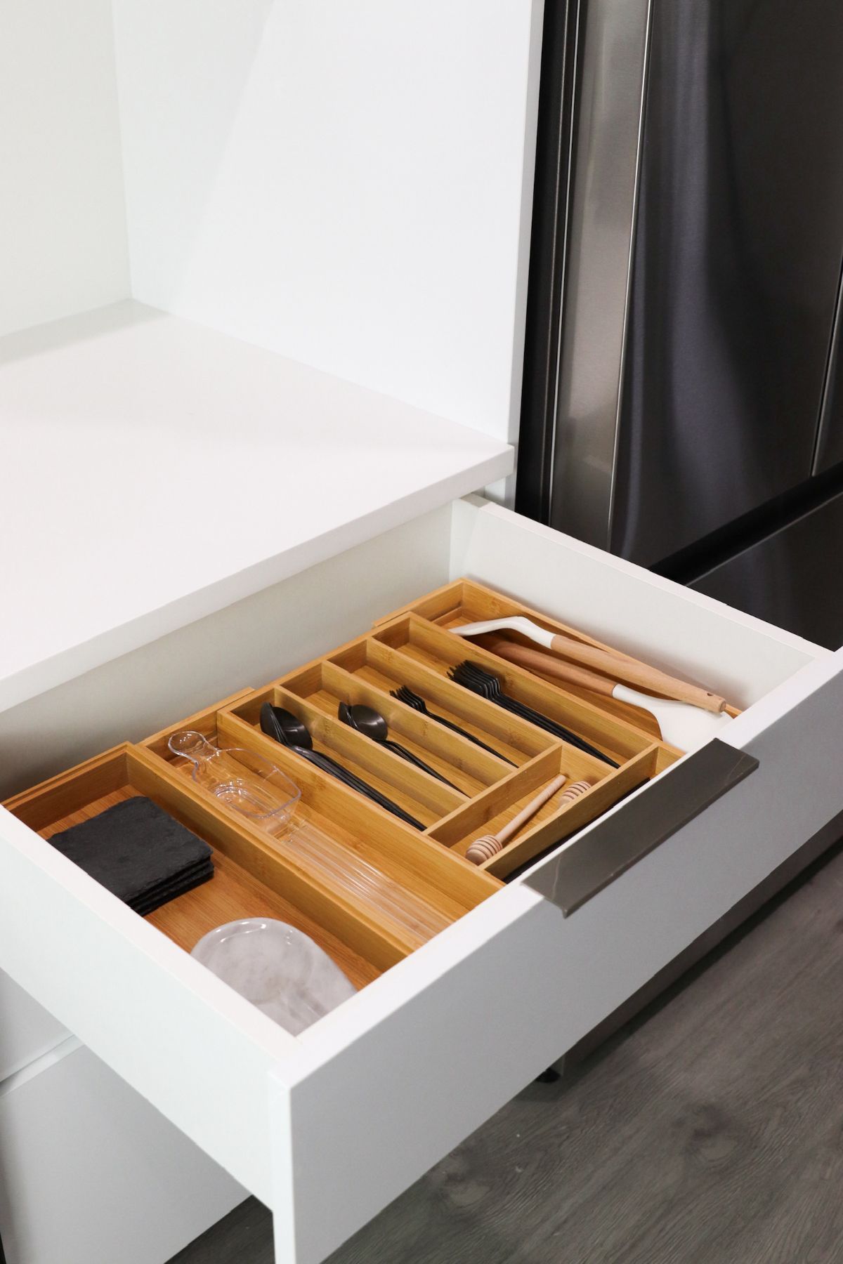 White kitchen drawer open with bamboo utensil organizer holding silverware.