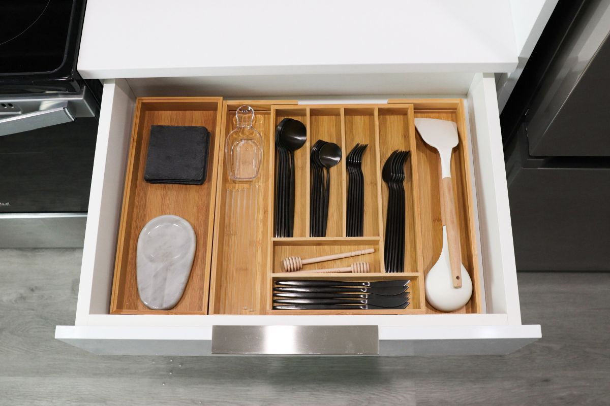 Open white kitchen drawer with bamboo utensil organizer, holding black utensils and a white spatula.