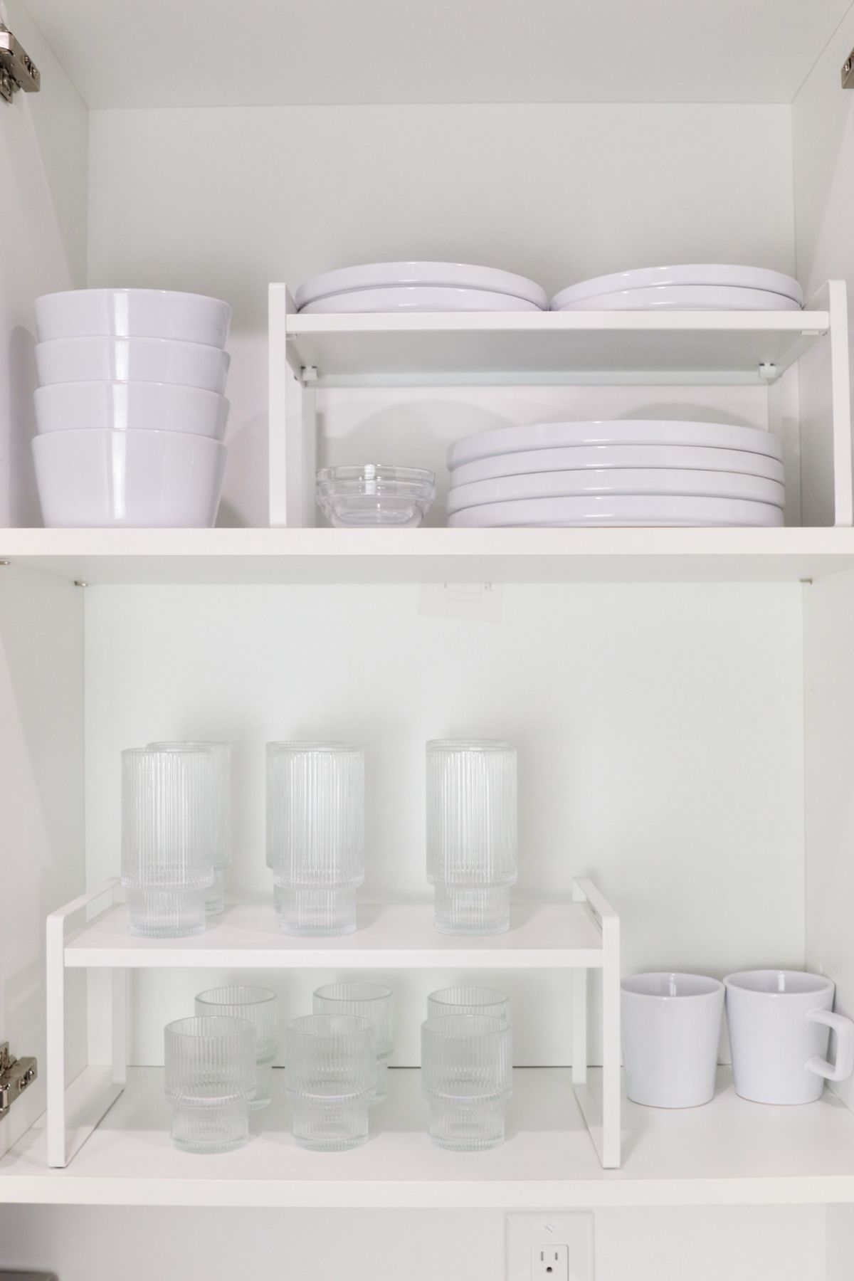 White kitchen cabinet with organized white dishes and glasses on shelves.