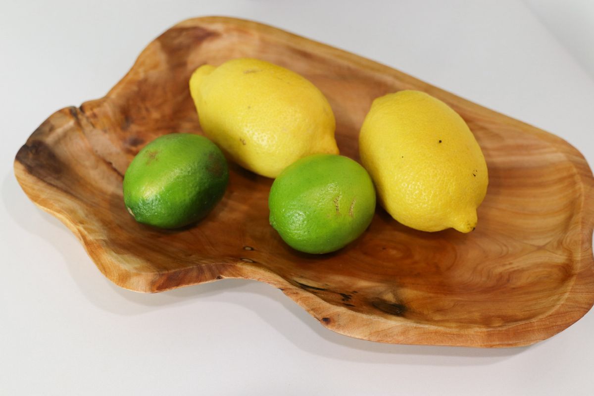 Lemons and limes in a rustic wooden bowl on a white surface.