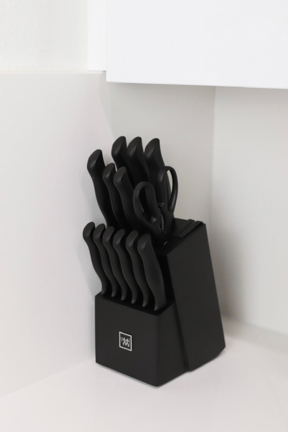 Black knife set in a black block on a white countertop, in the corner of a kitchen cabinet.