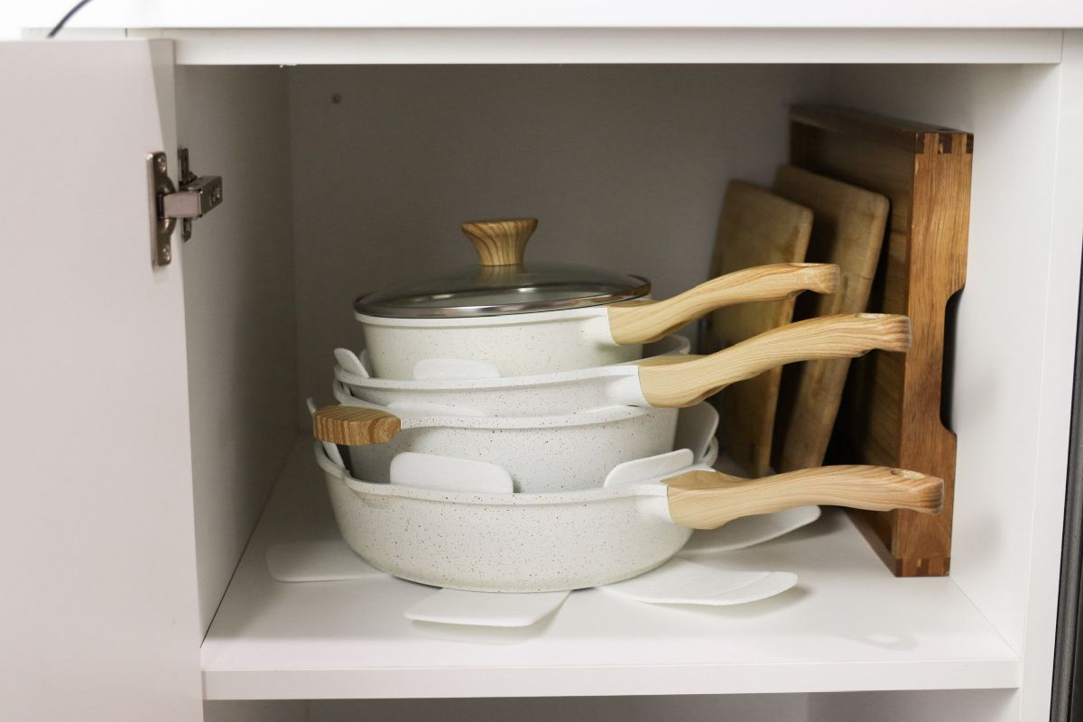 White cookware and wooden cutting boards stored in a white cabinet.