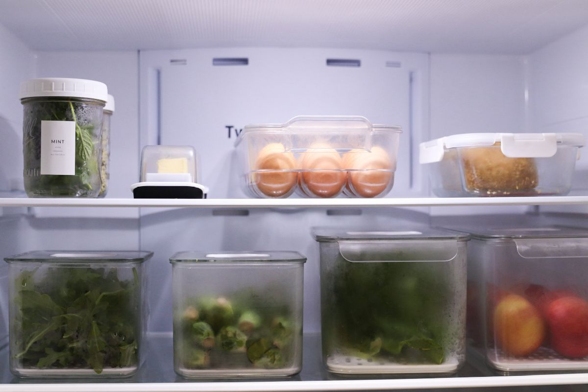 Refrigerator interior with various clear containers holding produce and eggs.