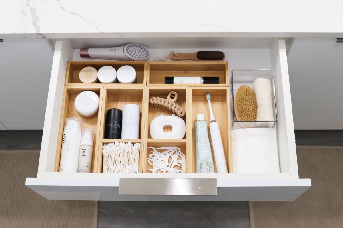 Organized bathroom drawer with bamboo dividers holding various toiletries, including a hairdryer and toothbrush.