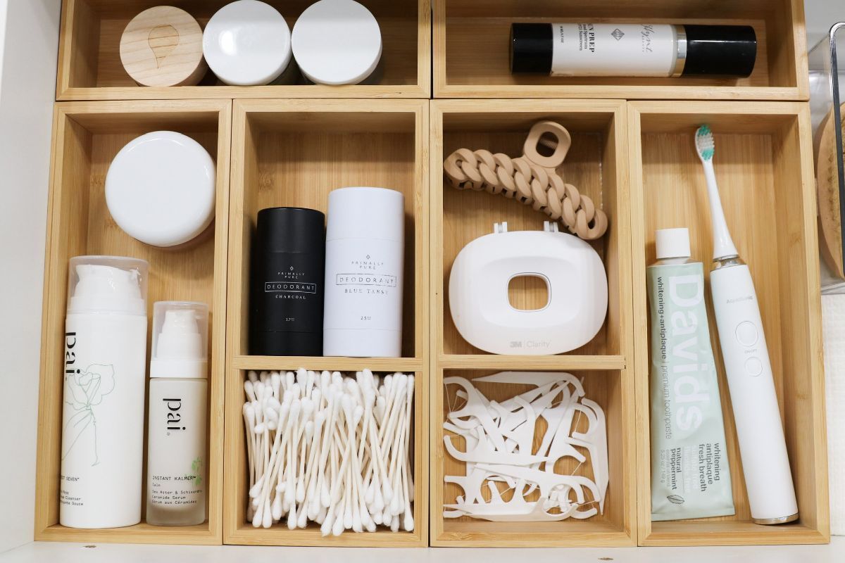 Wooden organizer drawer holding various bathroom products: skincare, hair accessories, dental hygiene items.