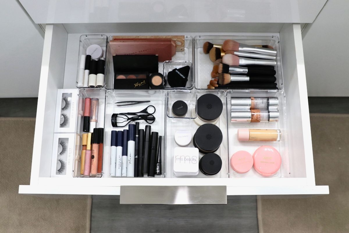 Open white drawer with organized makeup in clear containers.