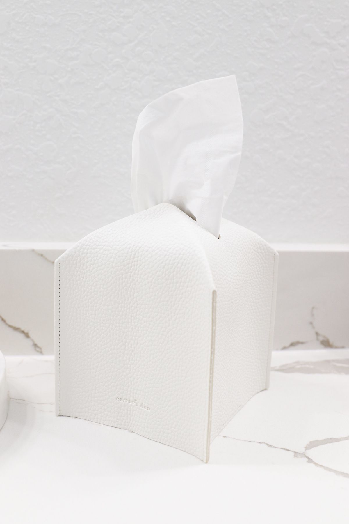 White tissue box with protruding white tissue on a white marble surface.