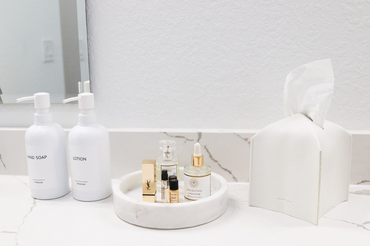 Bathroom counter with white bottles, a marble tray with perfume bottles, and a tissue box.