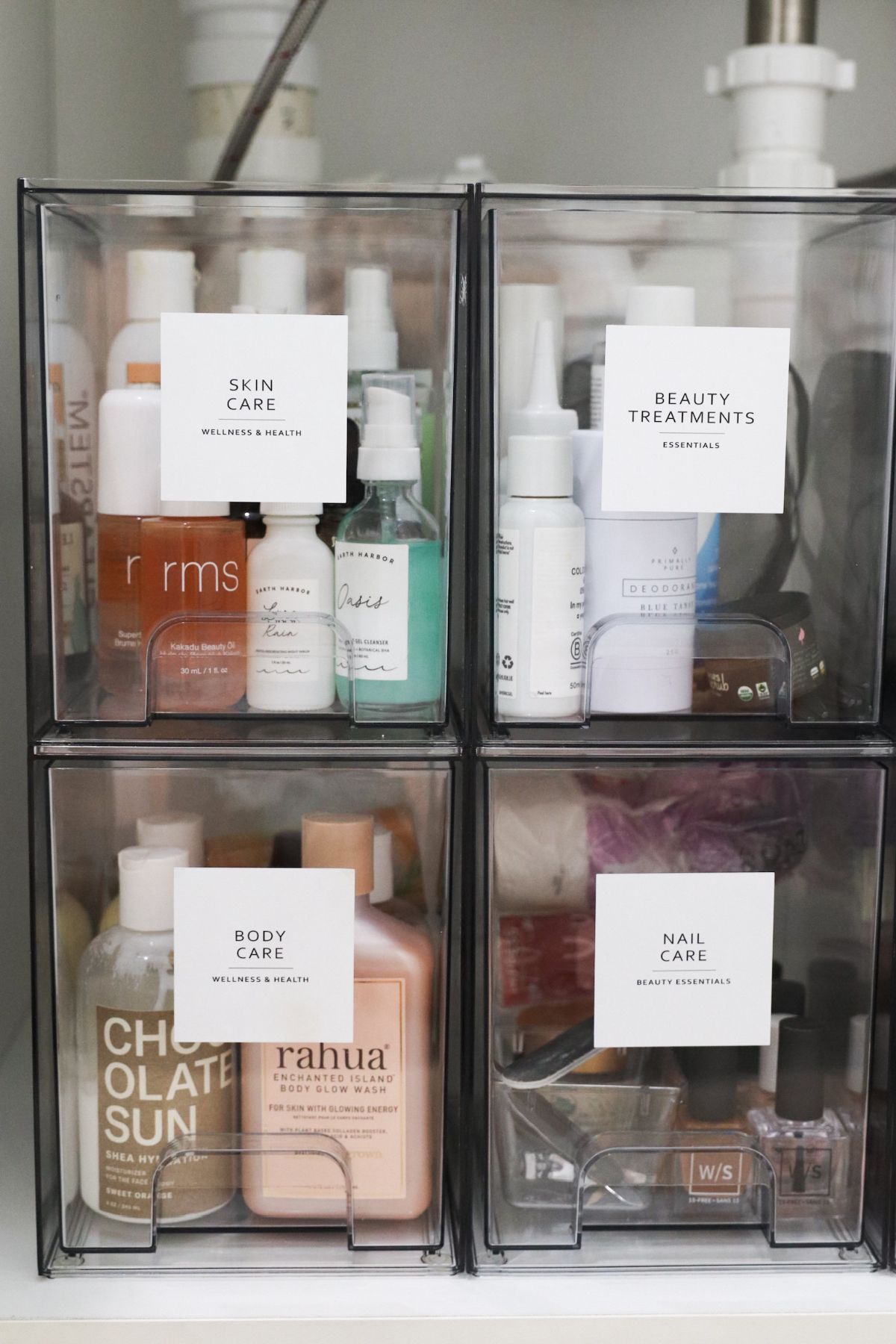 Four clear plastic bins organized with beauty products, labeled 