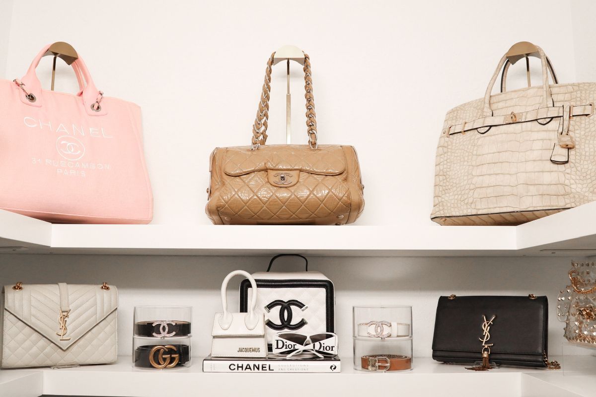 Shelves displaying luxury handbags, including pink, tan quilted, and beige bags.