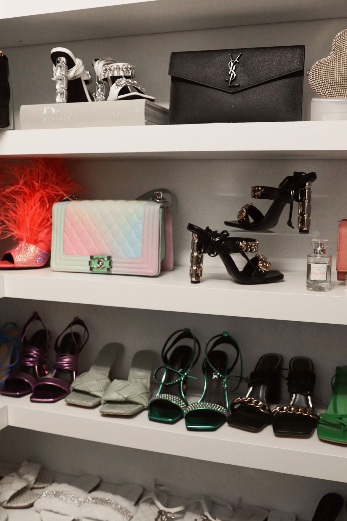 Closet shelves displaying luxury shoes and handbags in various colors.