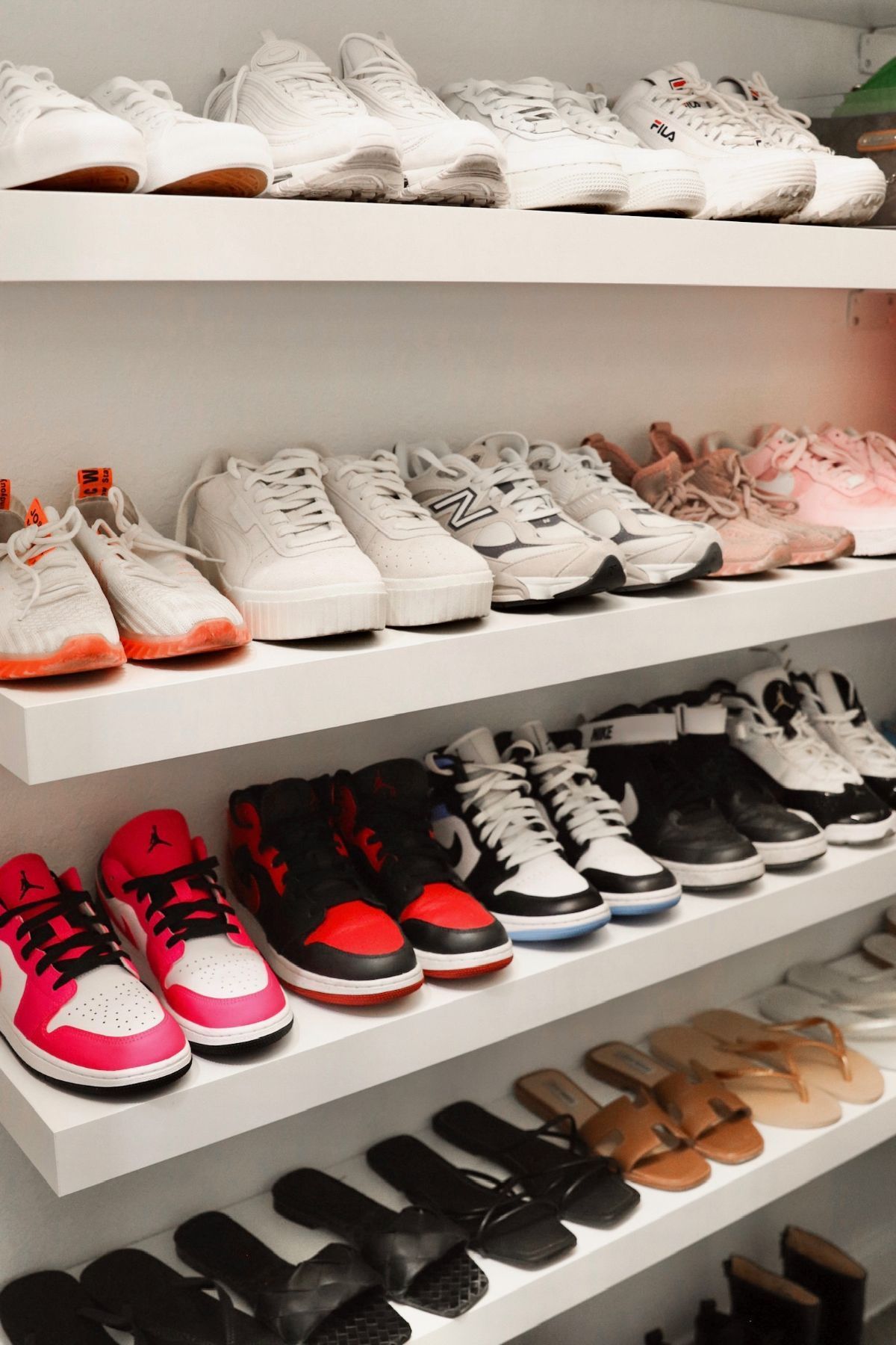White shelving displaying rows of sneakers, sandals, and slides.