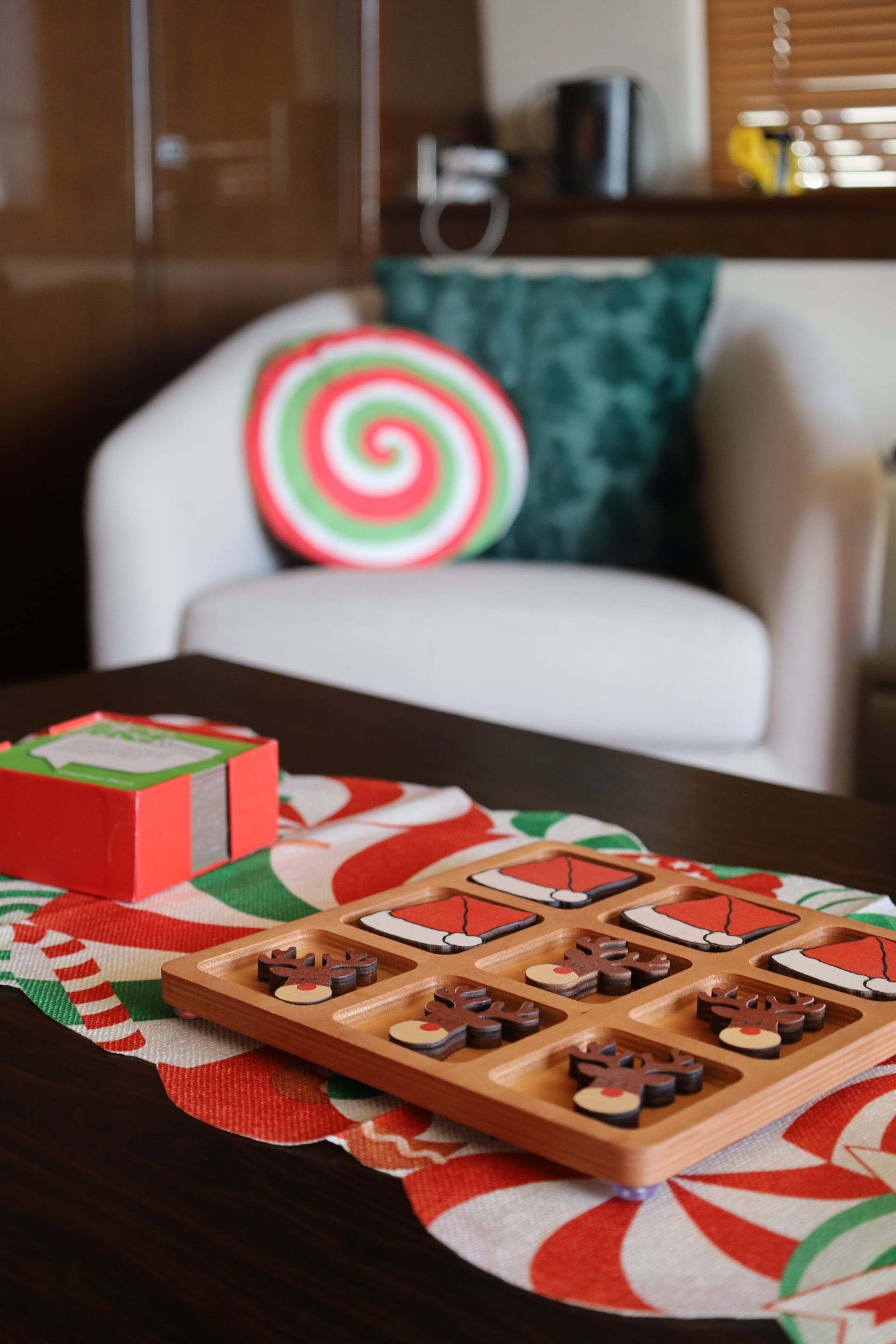 Christmas-themed coffee table with candy cane runner, wooden tray of cookies, and a peppermint swirl pillow on a white armchair.