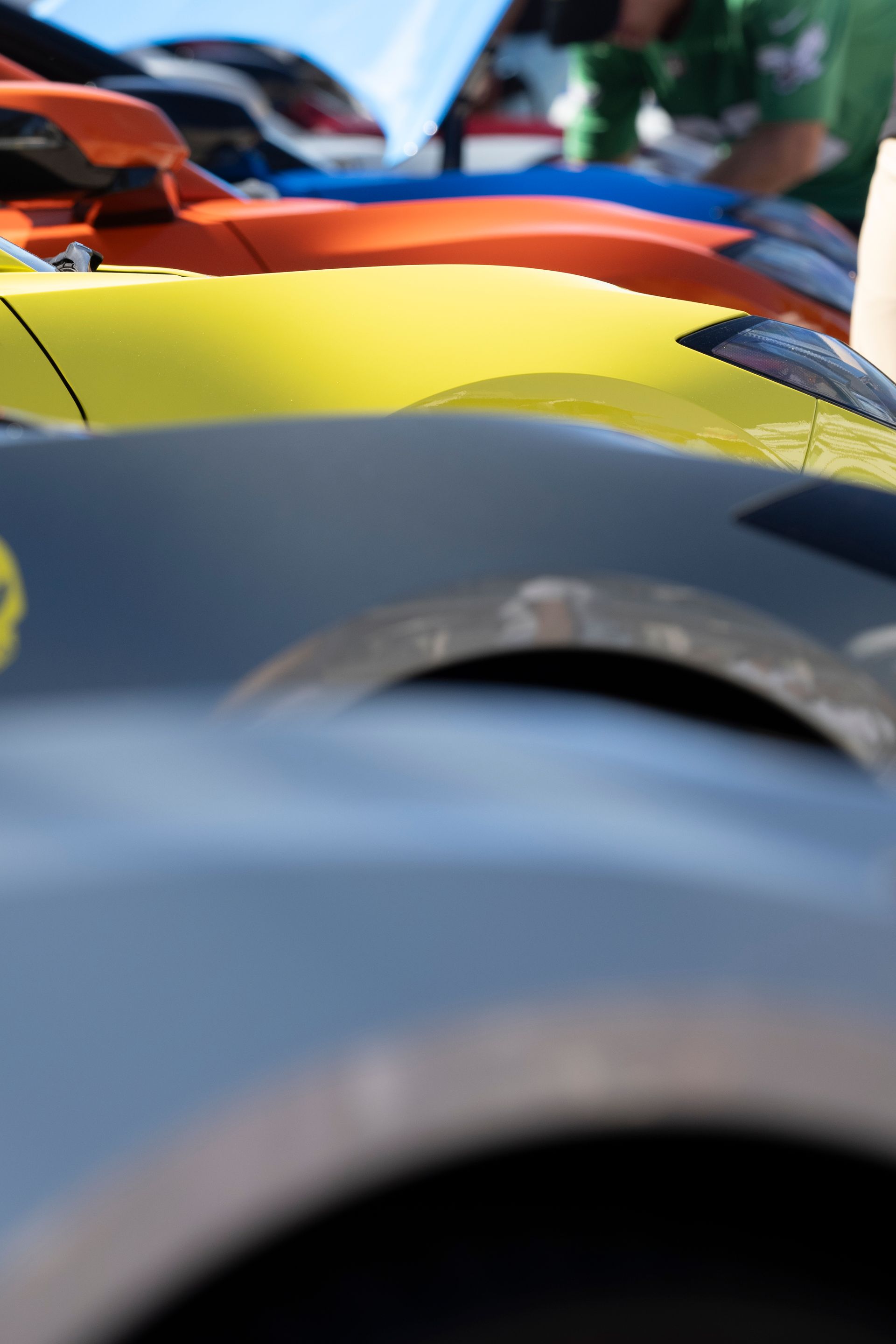 Close-up of a row of colorful sports car hoods: gray, yellow, orange and blue.