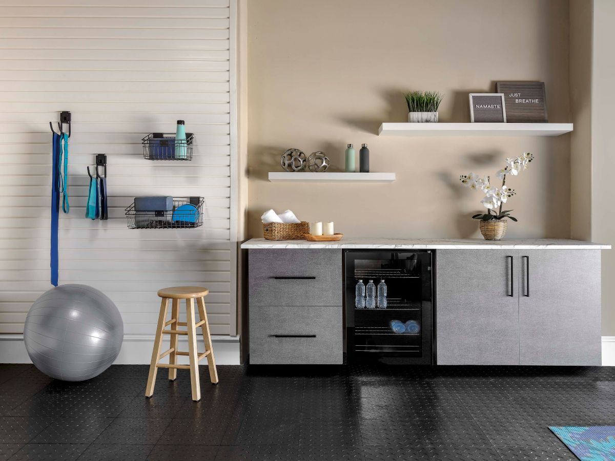 Home gym setup with storage and beverage cooler. Grey cabinets, white shelves, exercise equipment.