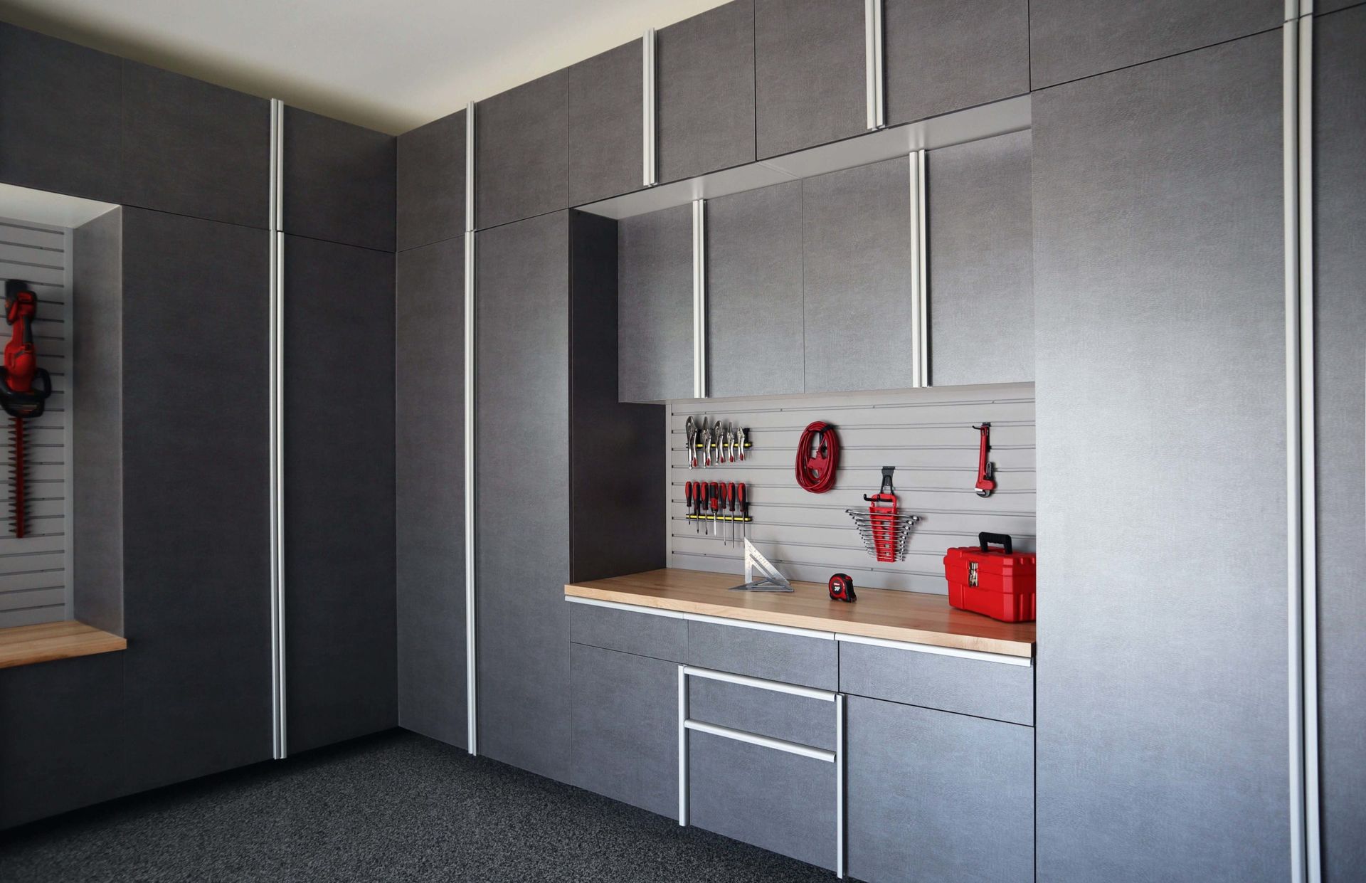 Modern dark grey garage storage cabinets with silver trim and a light wood workbench with mounted tool organization.
