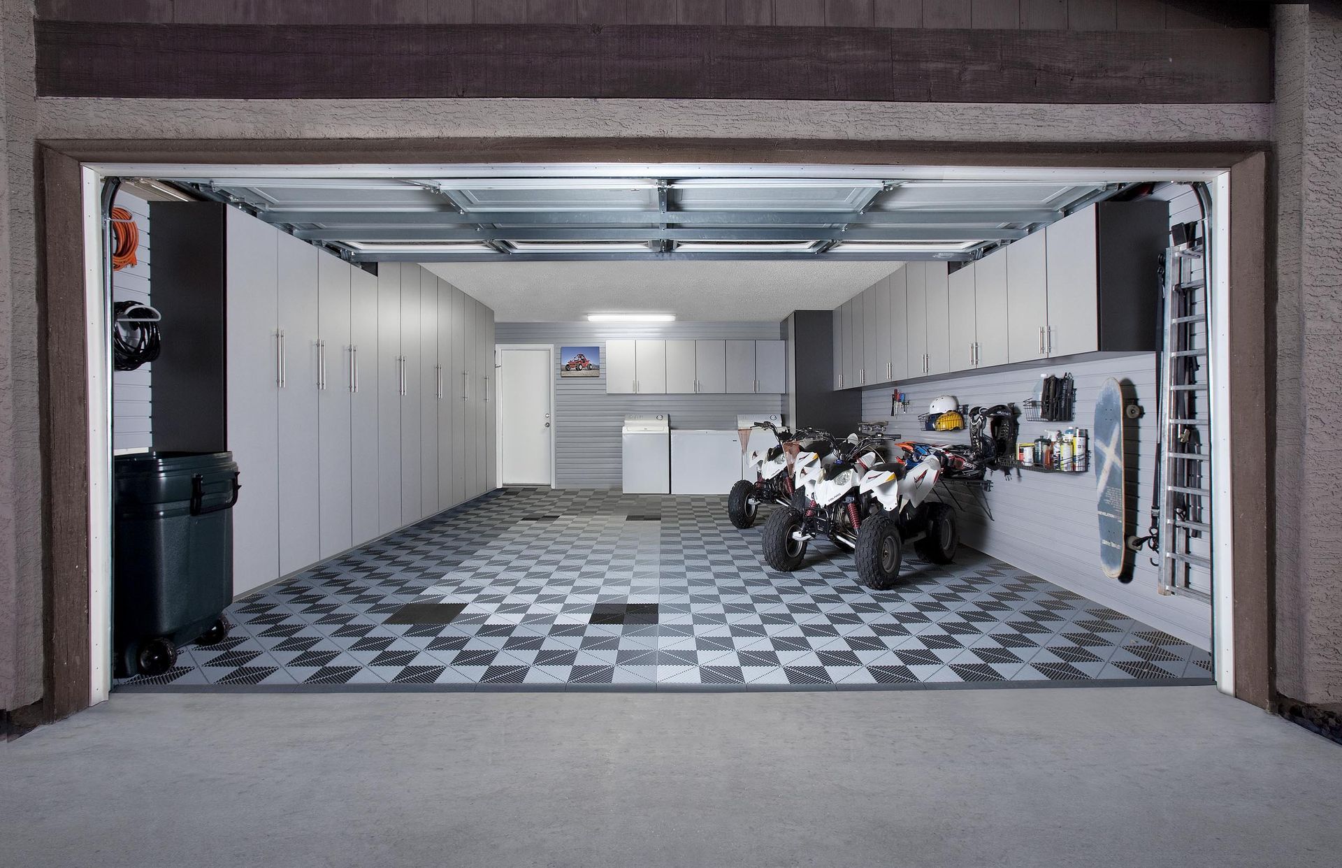 Open garage with a checkered Swisstrax flooring, storage cabinets, and two ATVs.
