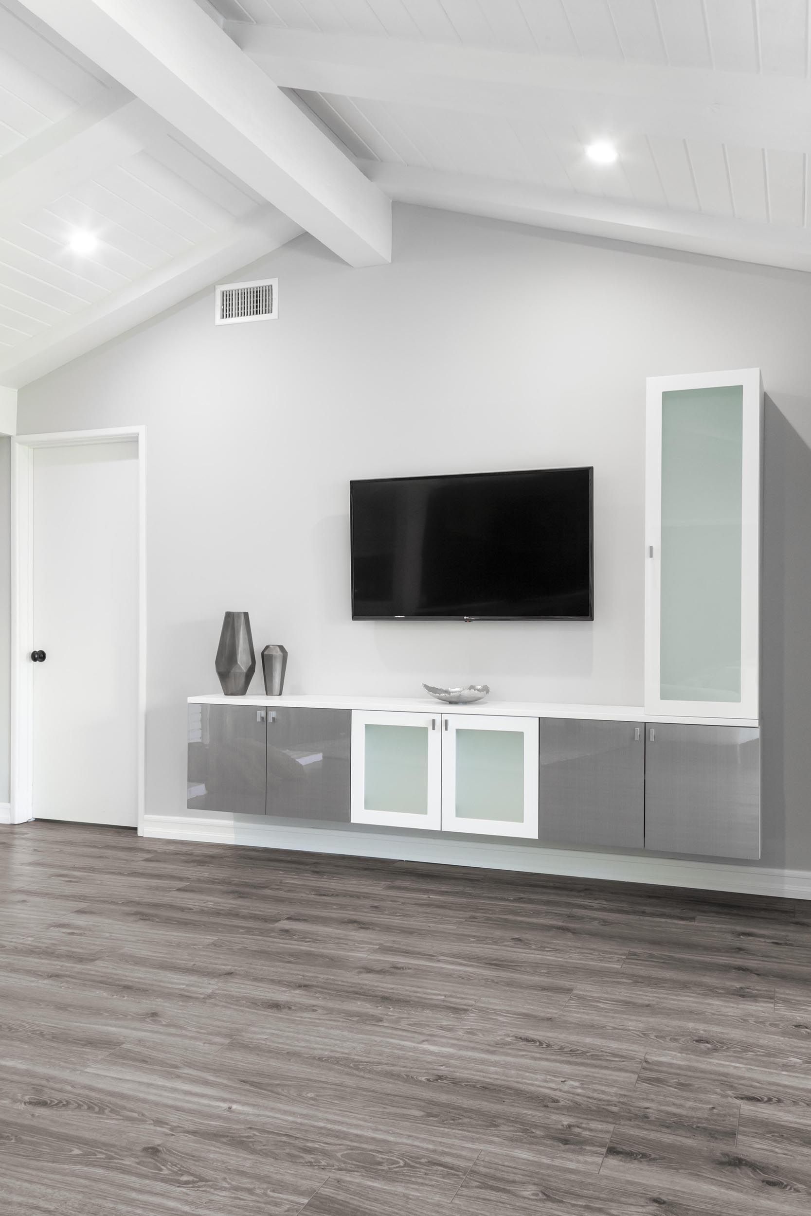 Modern living room with mounted TV, gray cabinets, and light gray walls.