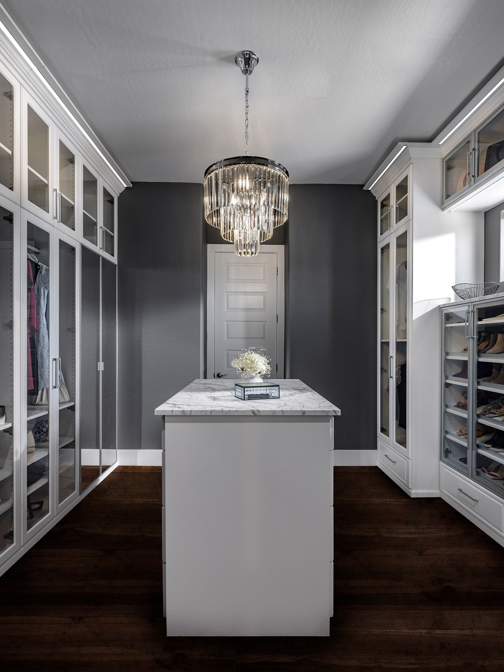 Walk-in closet with white cabinets, dark gray walls, a central island, and a chandelier.