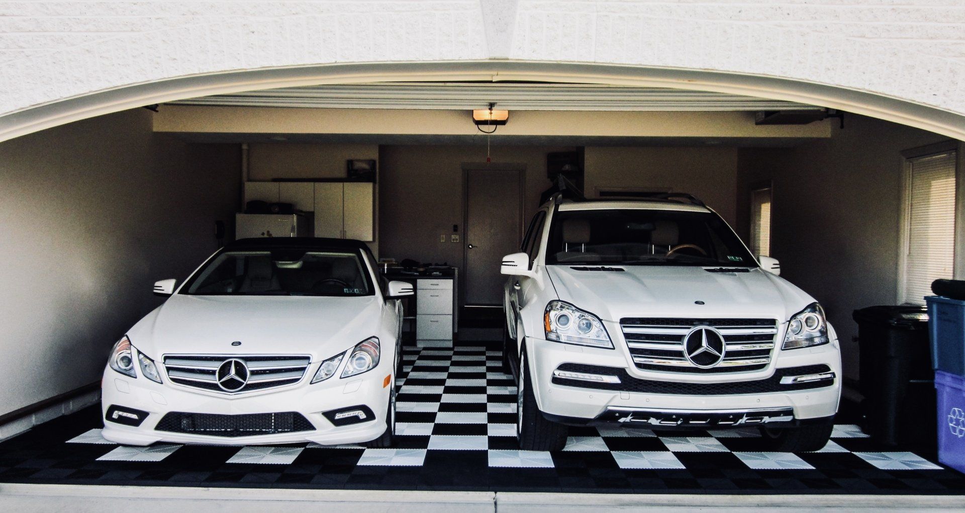 Two white Mercedes vehicles parked in a garage with checkered Swisstrax flooring.