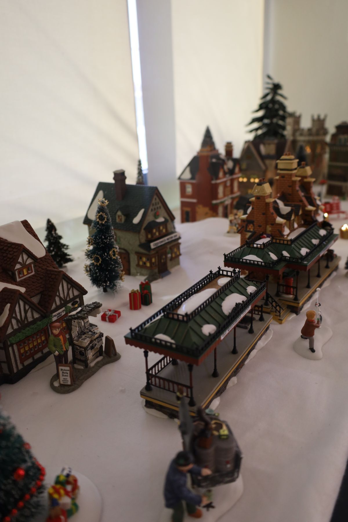 A Christmas village display with snow-covered buildings, a train station, and figurines.