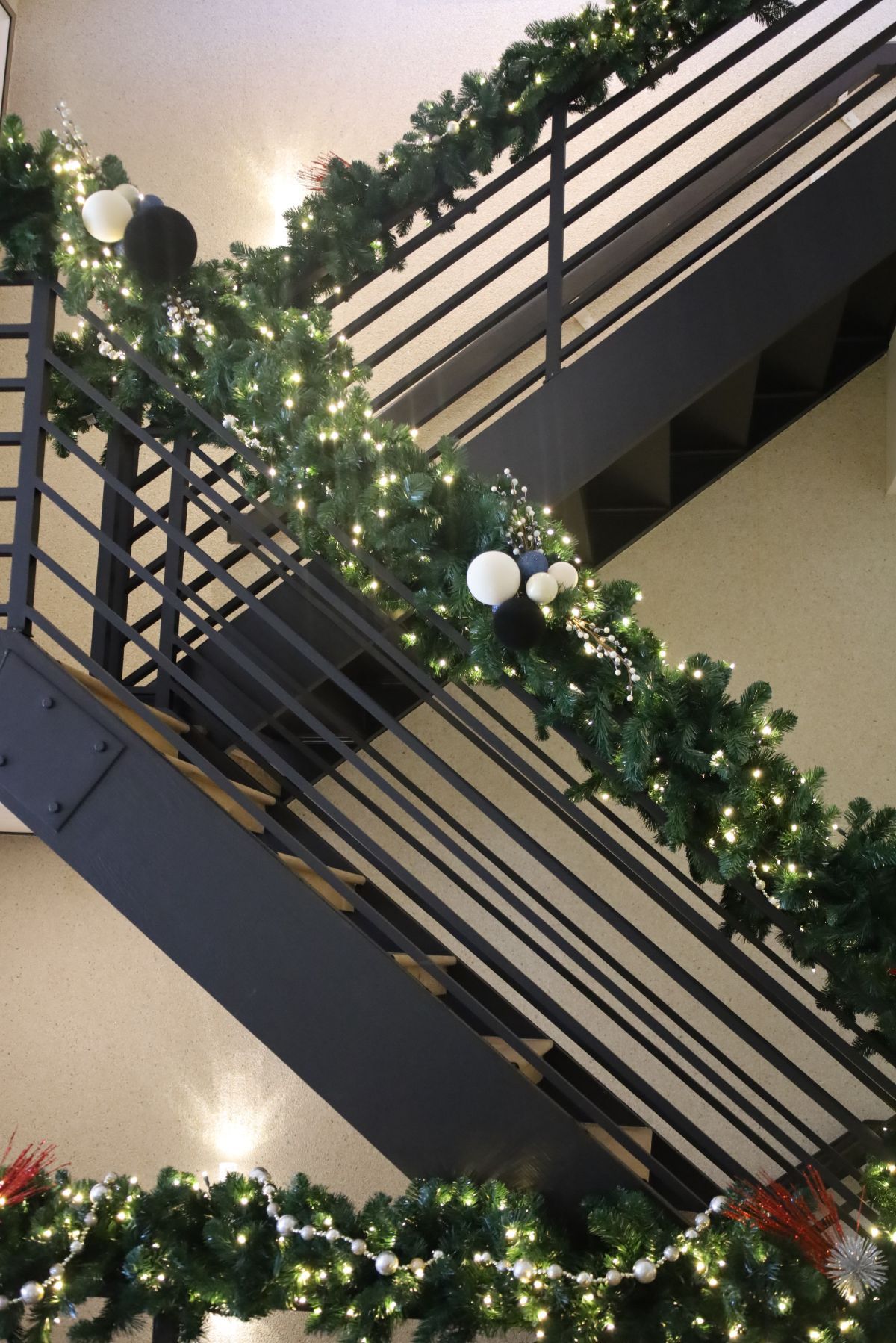 Staircase with black metal railings decorated with garland, lights, and ornaments.