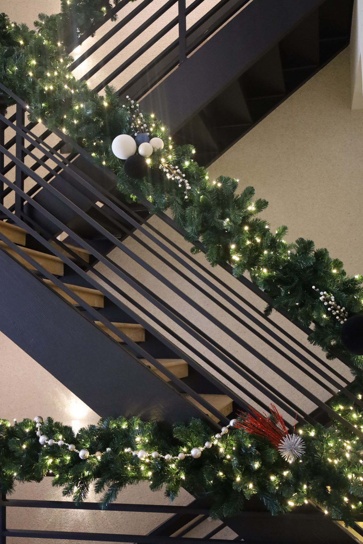 Staircase decorated with green garland, white lights, and ornaments, for the holidays.