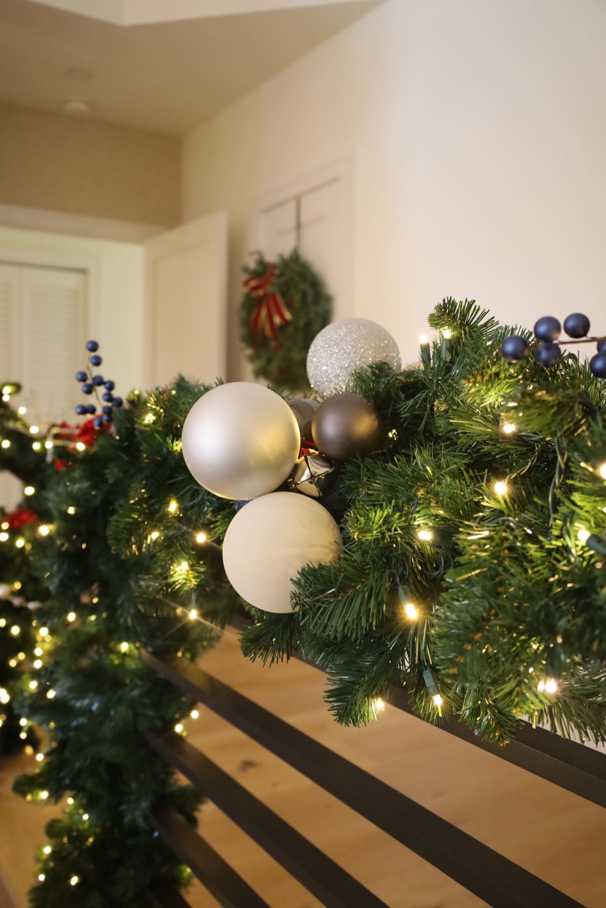 Christmas garland with ornaments and lights on a railing. A wreath hangs in the background.