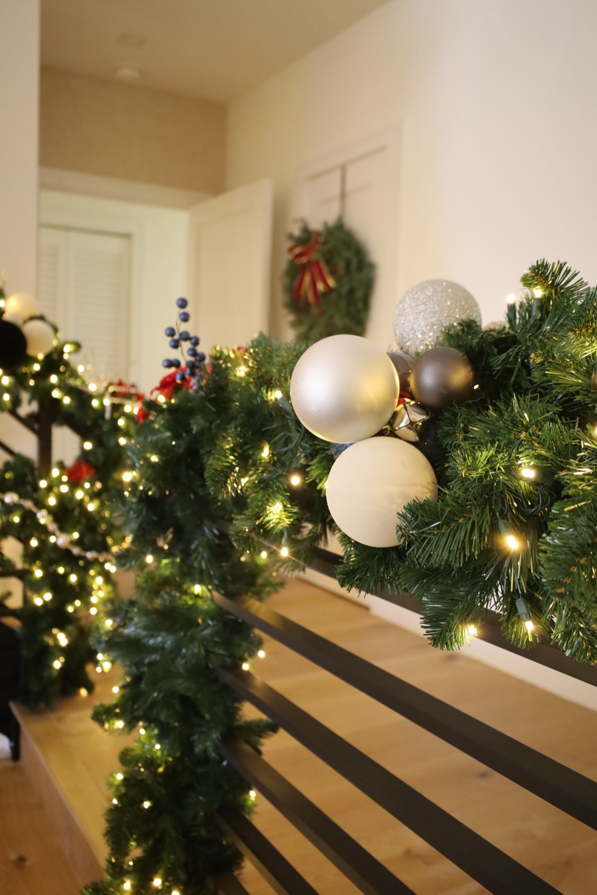 Christmas garland with ornaments and lights on a stair railing, with a wreath in the background.