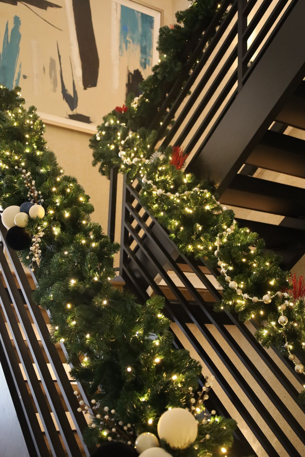 Christmas garland and lights decorate a stairwell with black railings, adorned with ornaments and artwork.