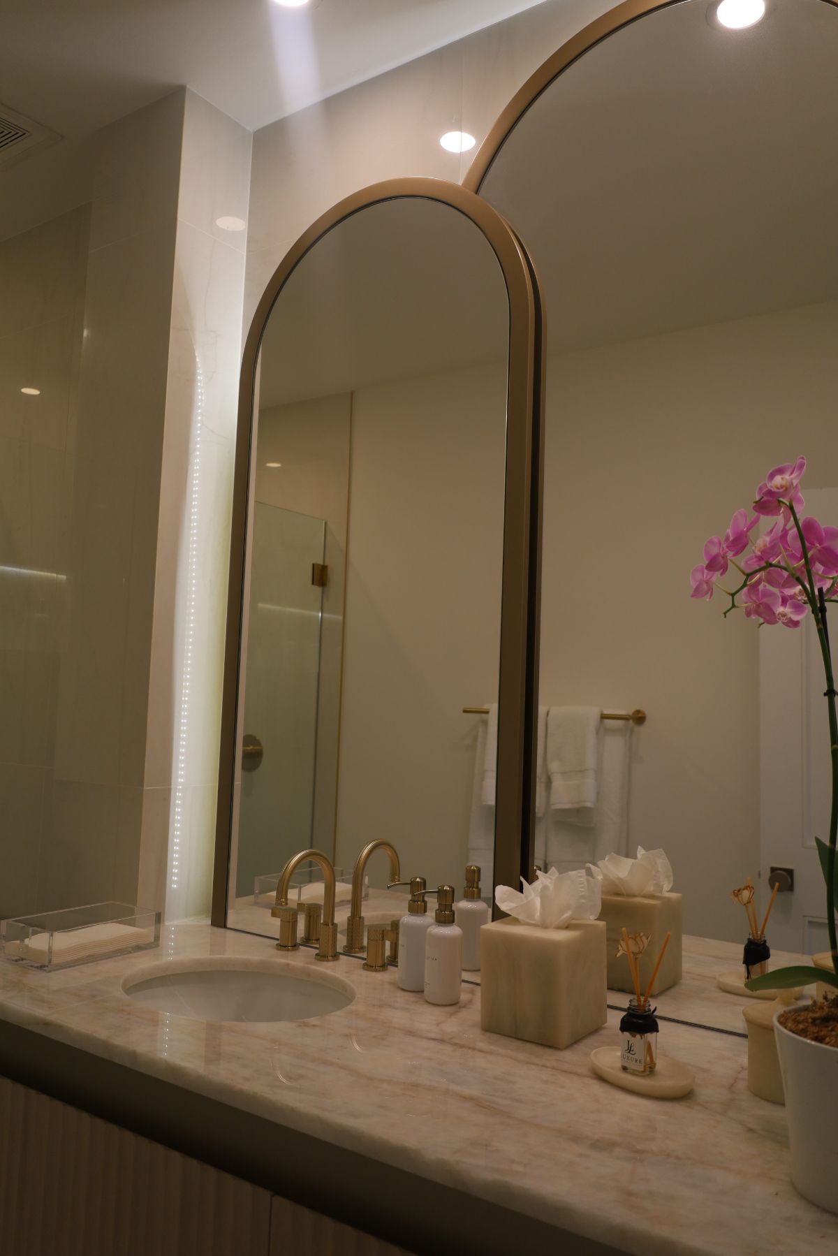 Bathroom with arched mirrors, gold fixtures, marble countertop, and pink orchid.