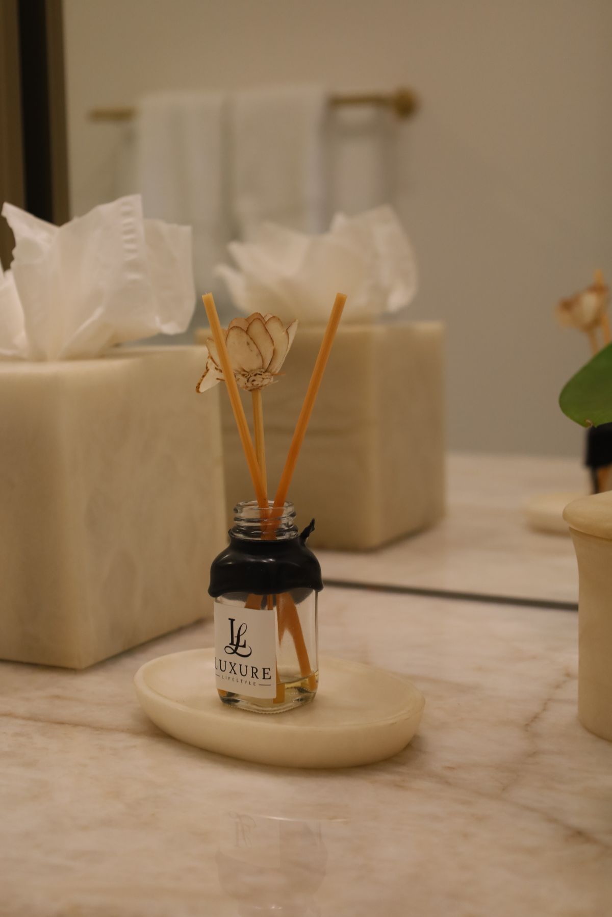 Reed diffuser on a marble countertop with tissues and mirror reflection.