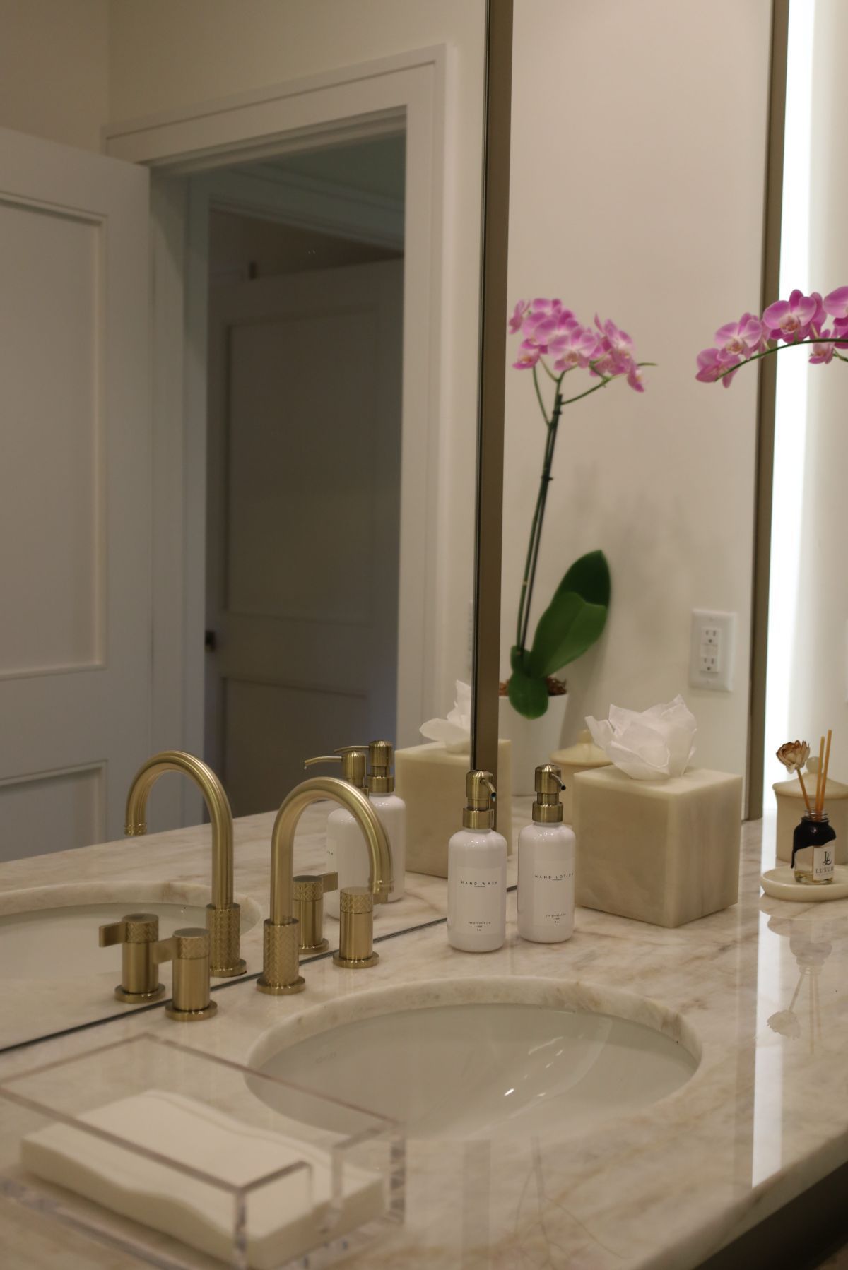 Bathroom with marble countertop, gold fixtures, and orchid flowers.