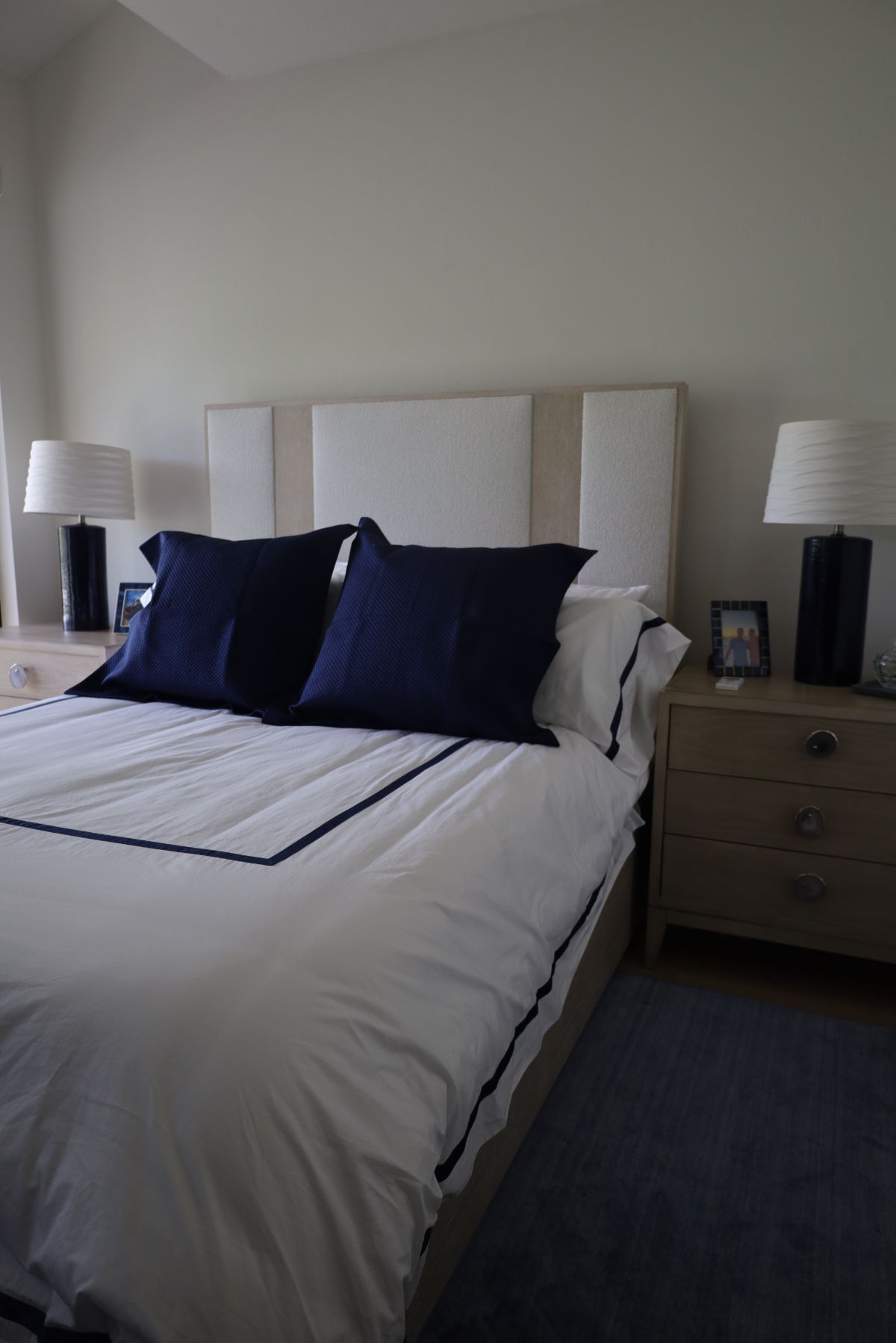 Bedroom with white bedding, navy blue pillows, and bedside lamps.
