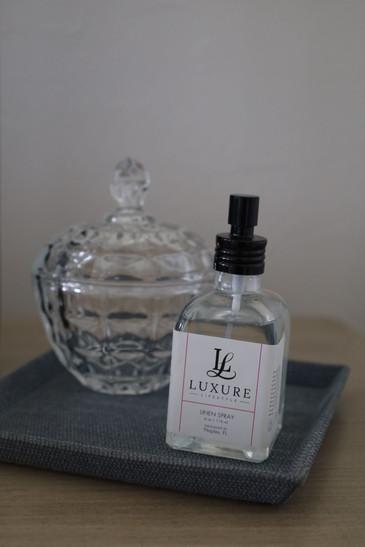 Glass perfume bottle and decorative dish on a gray tray, against a light wall.