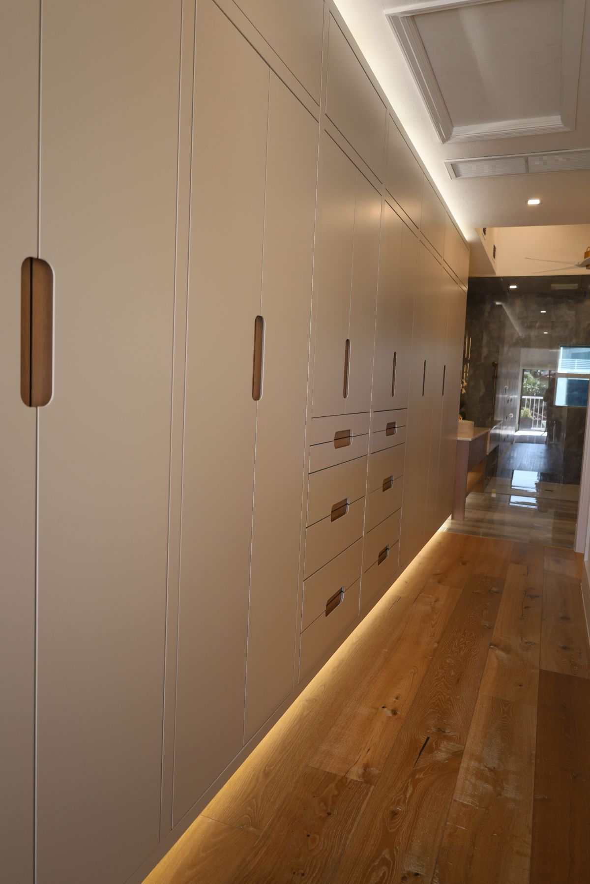 Long hallway with light wood floor and light-colored built-in cabinets with wood handles.