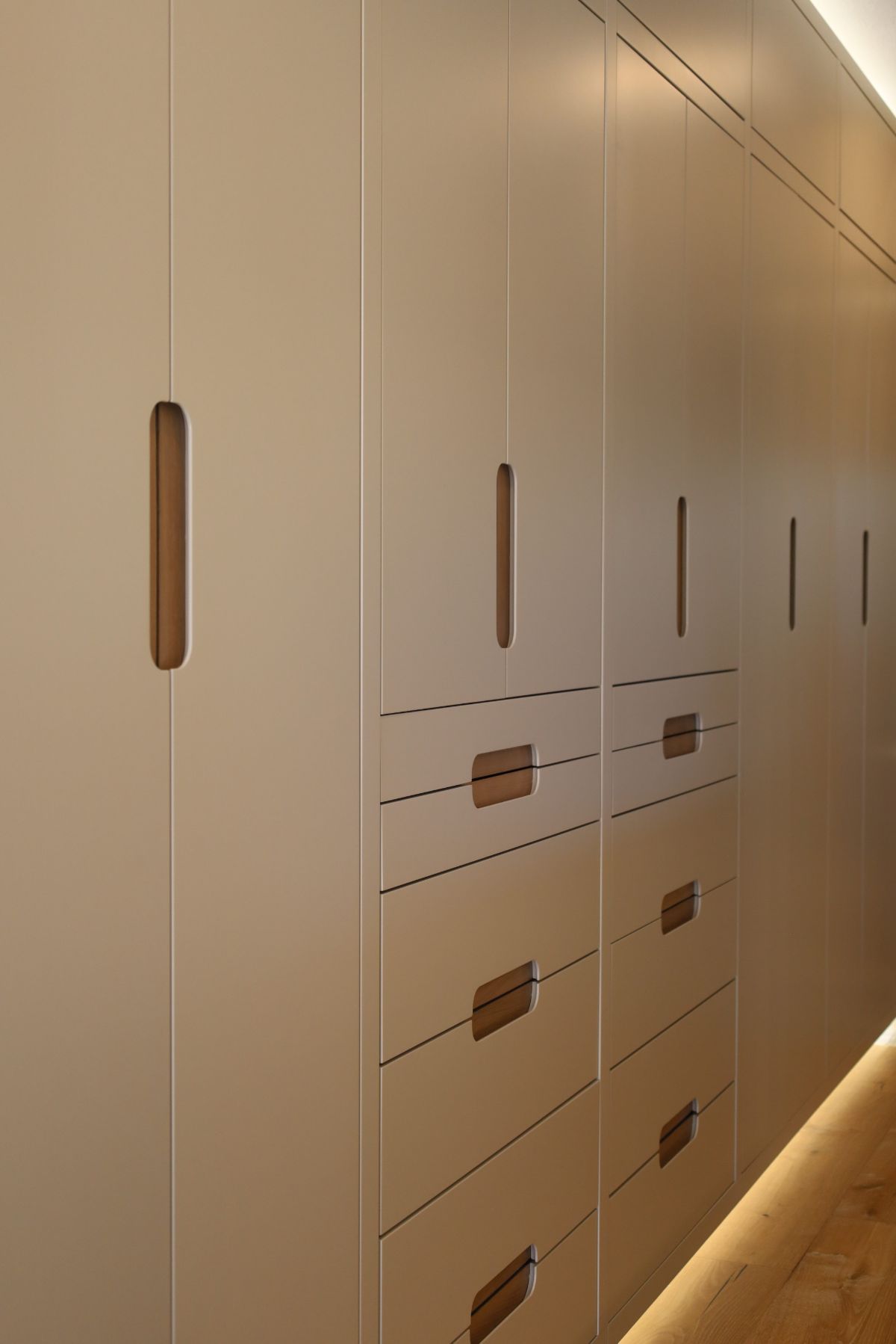 Beige built-in cabinets with wood handles, vertical and horizontal, in a hallway.