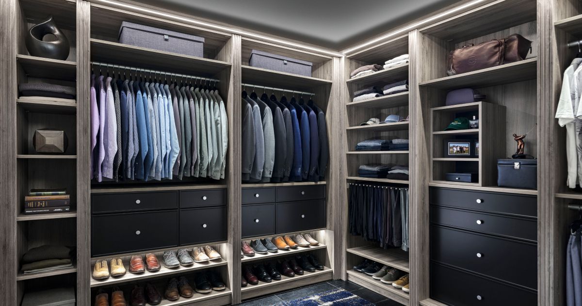 Walk-in closet with organized clothing, shoes, and drawers in neutral tones, illuminated by overhead lighting.