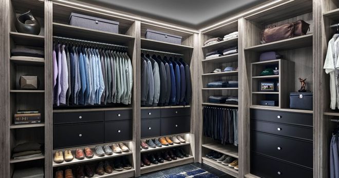 Walk-in closet with organized clothing, shoes, and drawers in neutral tones, illuminated by overhead lighting.