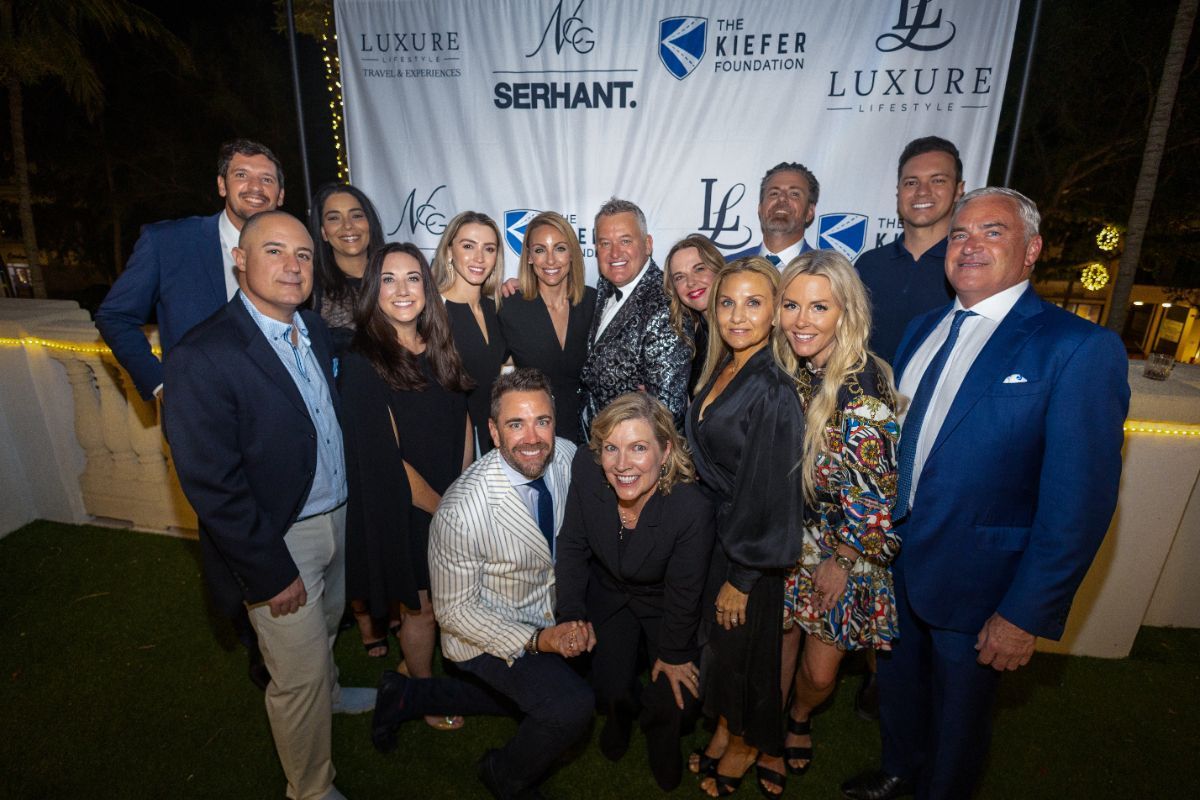 Group photo at an event; people posing in front of a branded backdrop, some smiling.