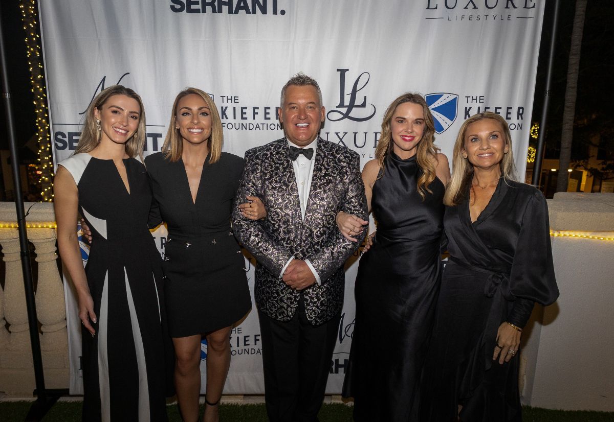 Five people smiling and posing in front of a white banner at an outdoor event.