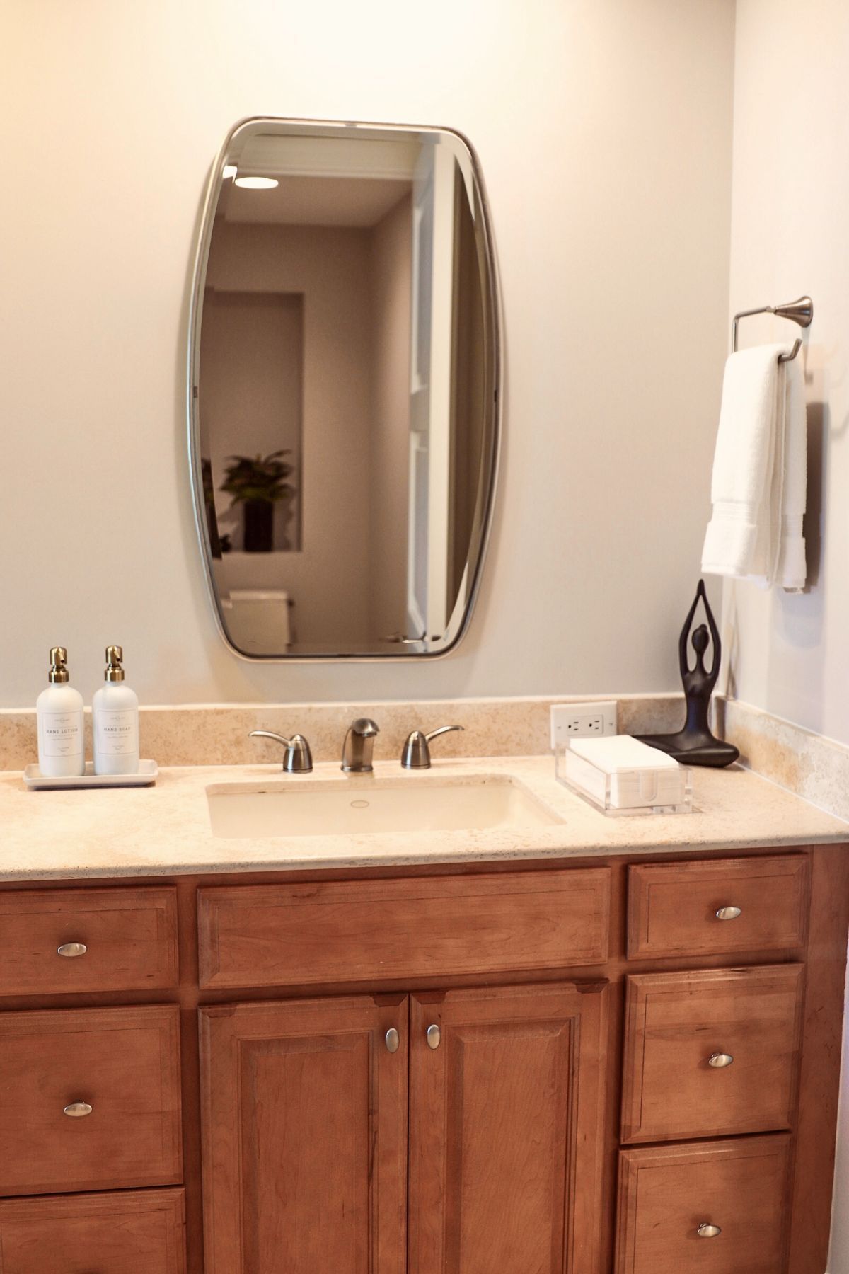 Bathroom vanity with a mirror, sink, and wooden cabinets. Beige countertop, light walls, and towel rack.
