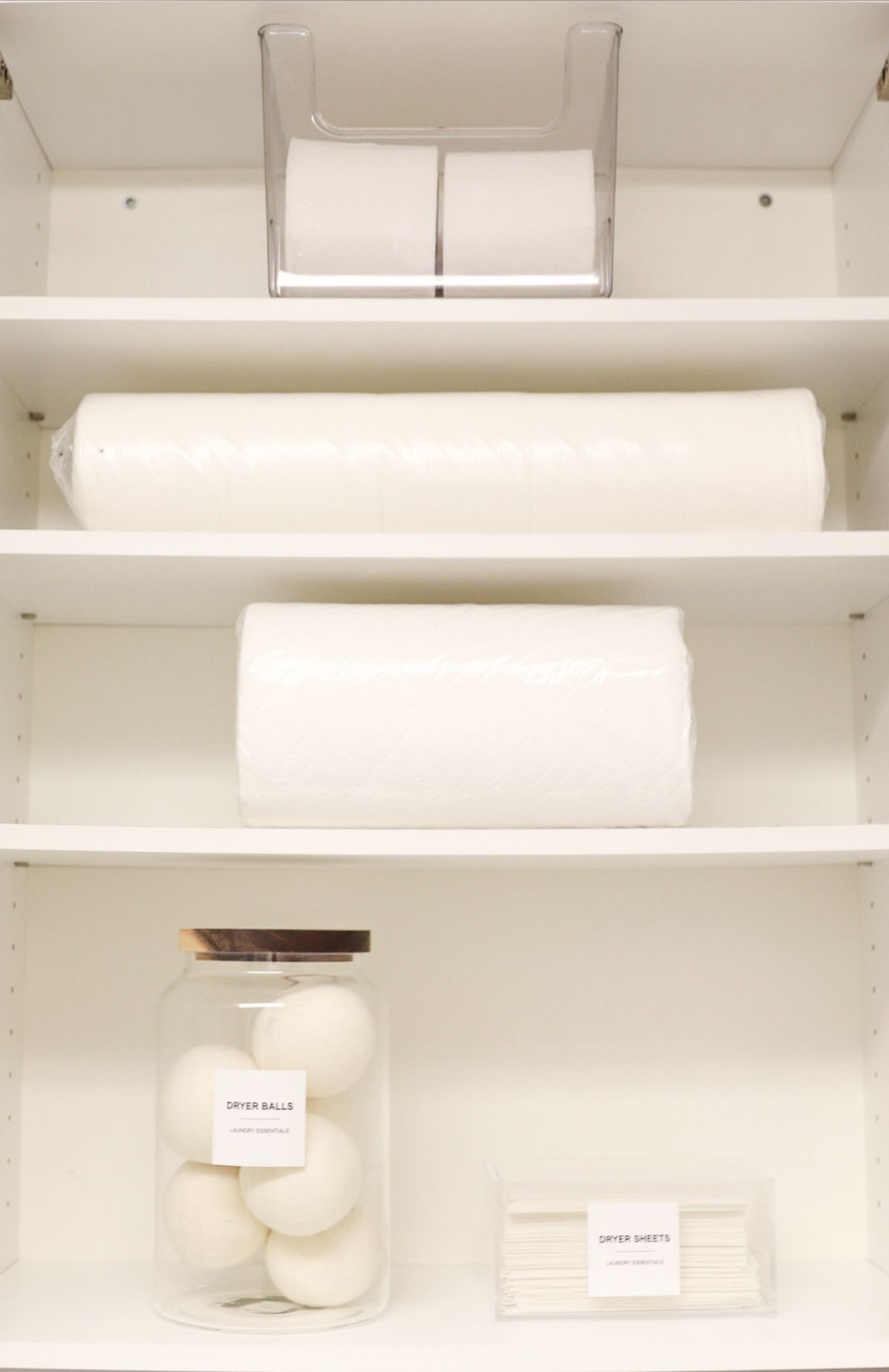A white cabinet with shelves holding toiletries: toilet paper, paper towels, cotton balls, and soap.