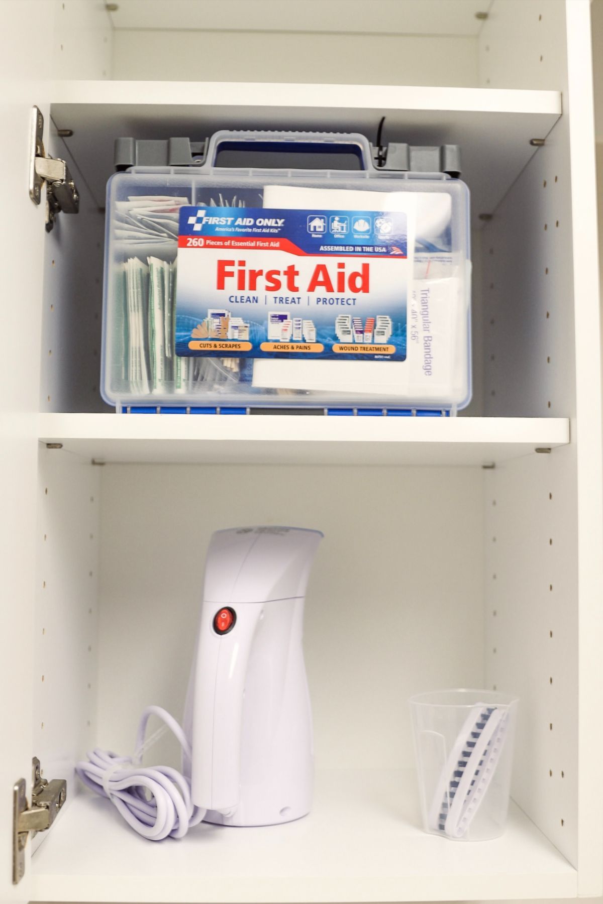 A first aid kit sits on a shelf above a humidifier and accessories in a white cabinet.